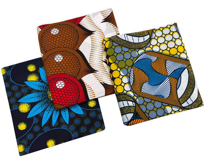 African wax print patterns, displayed overlapping on a solid white background. The patterns feature geometric shapes, floral motifs, and abstract designs in brown, blue, yellow, red, black, and white.