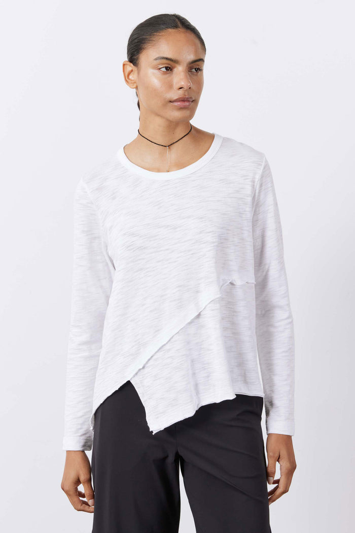 White asymmetric long sleeve top on model with uneven hem and crew neckline